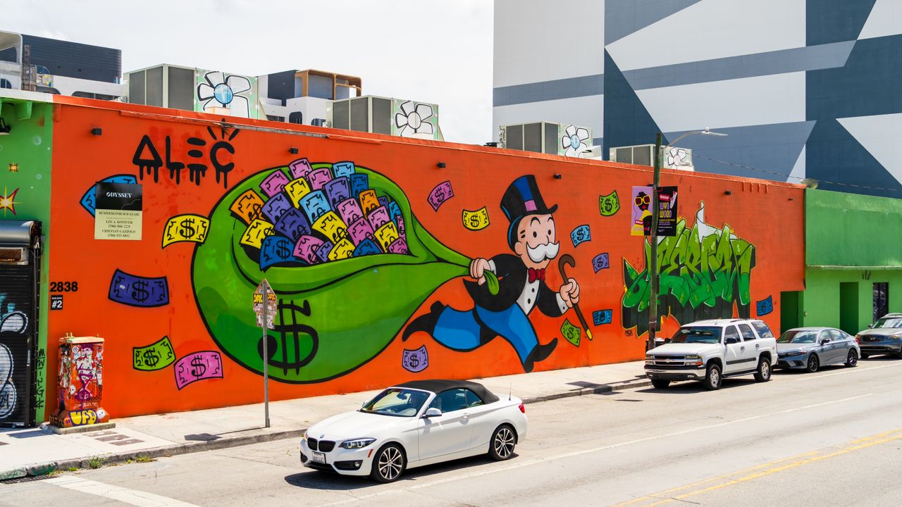 Colorful graffiti of Monopoly character on a street wall in Miami Design District with parked cars.