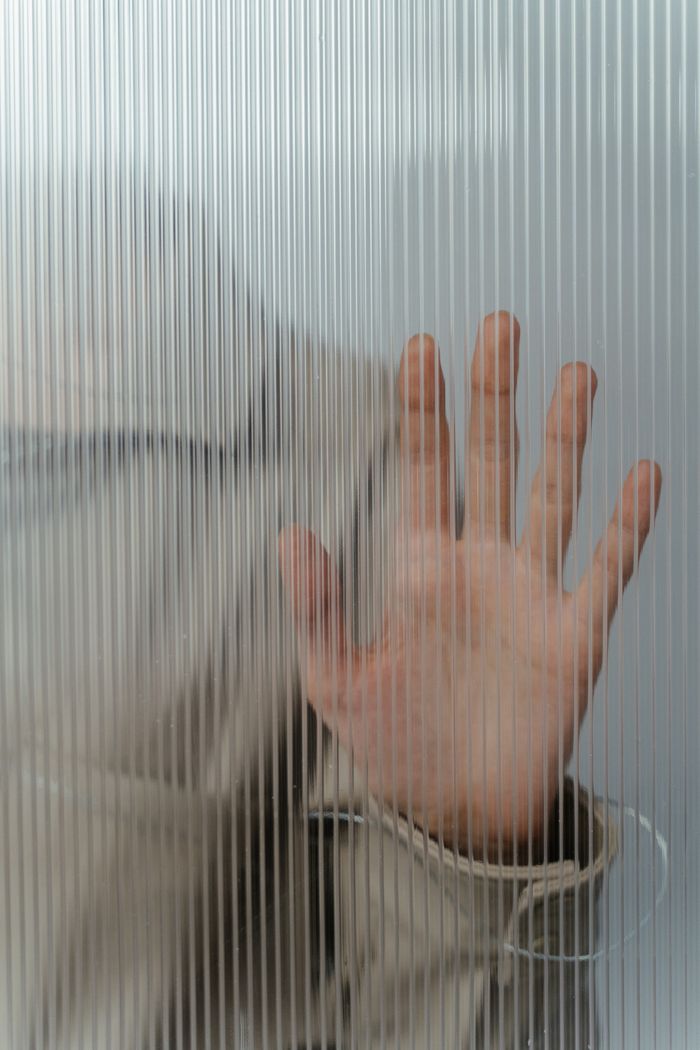 Close-up of a human hand pressed against frosted glass with vertical lines for an abstract and contemporary effect.